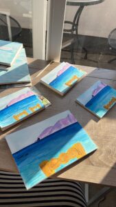 Four sketchbooks with the painting of the back of a chair in front of the sea with an island in the distance