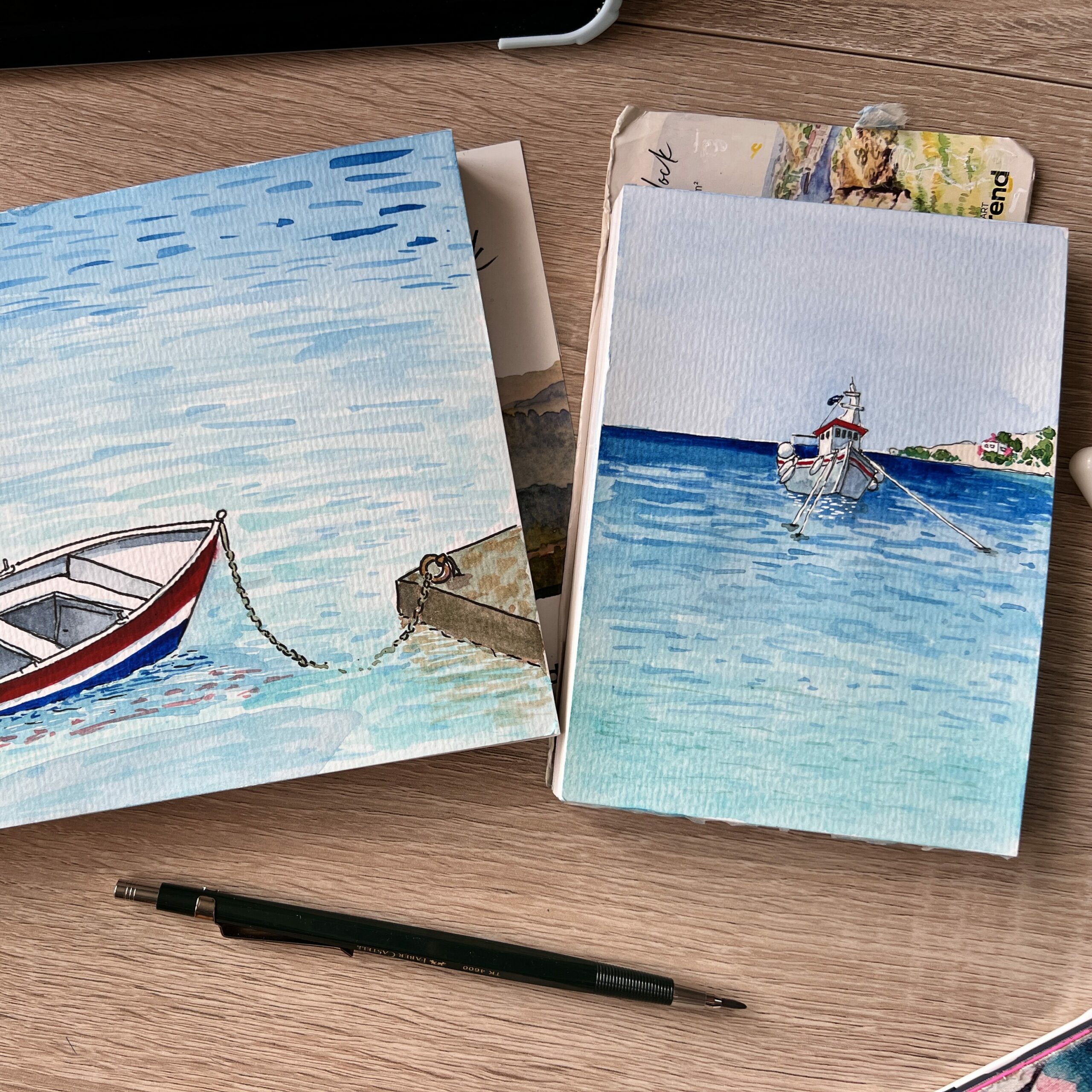 two sketchbooks, each with a tiny painting of a boat on the sea